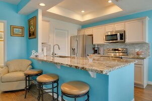 A kitchen with a marble countertop, stainless steel appliances, and a bar stool seating area.