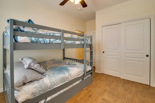 A bunk bed with patterned bedding, a ceiling fan, and a white door in a room with wooden flooring.