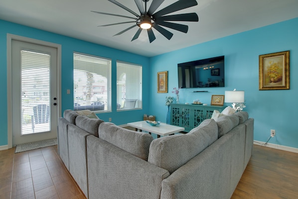 A living room with a sectional sofa, a ceiling fan, a television, and a cabinet. - Waterfront Unit w/ Resort Perks in Laguna Vista! (Port Isabel)