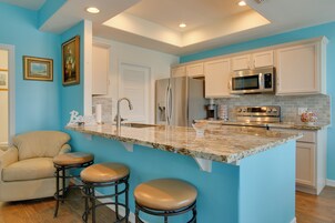 A kitchen with a marble countertop, stainless steel appliances, and a bar stool seating area.