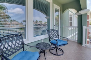A balcony with two chairs and a small table, overlooking a residential area with palm trees.