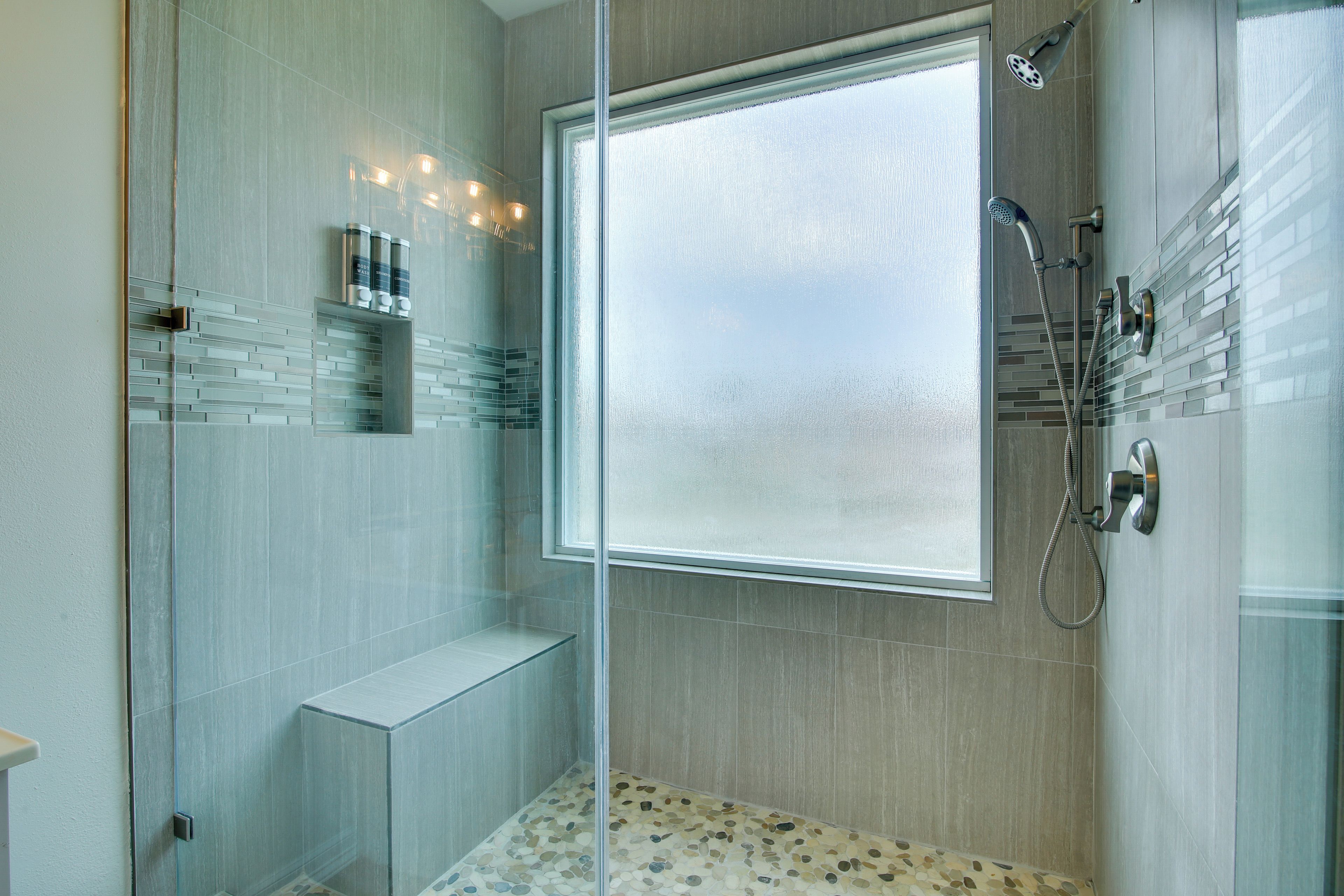 Une salle de bain moderne dotée d’une cabine de douche en verre, d’un banc intégré et d’une grande fenêtre à vitrage dépoli.