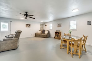 A spacious living area with a ceiling fan, a sofa, a dining table with chairs, and a cross on the wall. - Great for Families! Fredericksburg Home w/ Hot Tub (Fredericksburg)