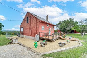 A red wooden house with a porch, a fenced yard, and a small play area with a slide and a turtle-shaped play structure. - Great for Families! Fredericksburg Home w/ Hot Tub (Fredericksburg)