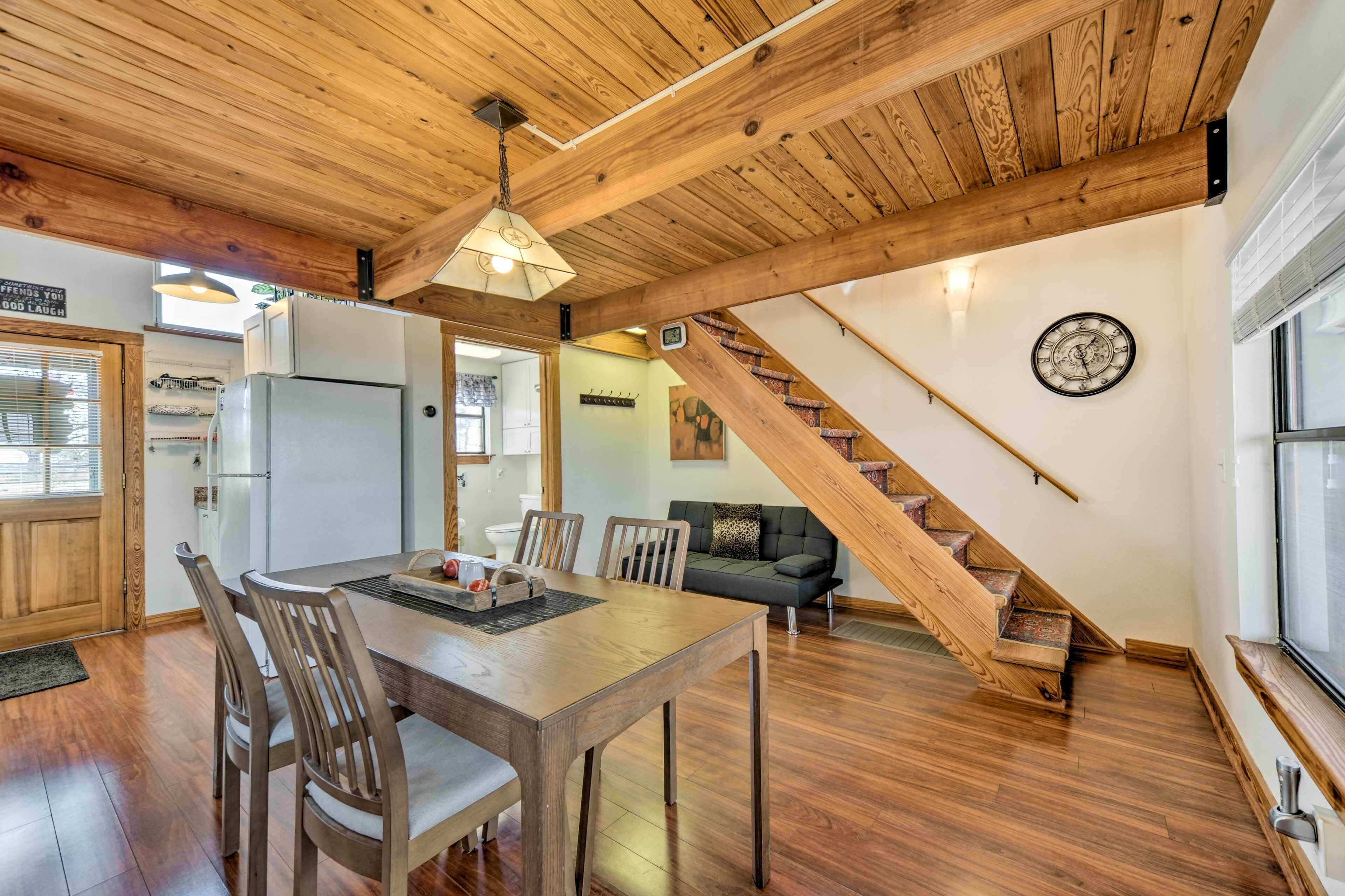 Una cocina amplia con vigas de madera, un comedor con mesa y sillas de madera, y una escalera que sube a otro nivel.