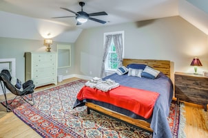 Un dormitorio con cama, ventilador de techo, cómoda, silla, ventana con cortinas y una alfombra estampada.