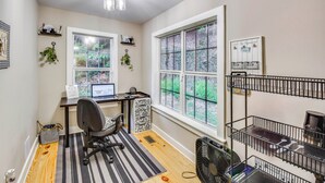 Ein Zimmer mit Schreibtisch, Stuhl, Computer, Fenster, Heizkörper und Ventilator.