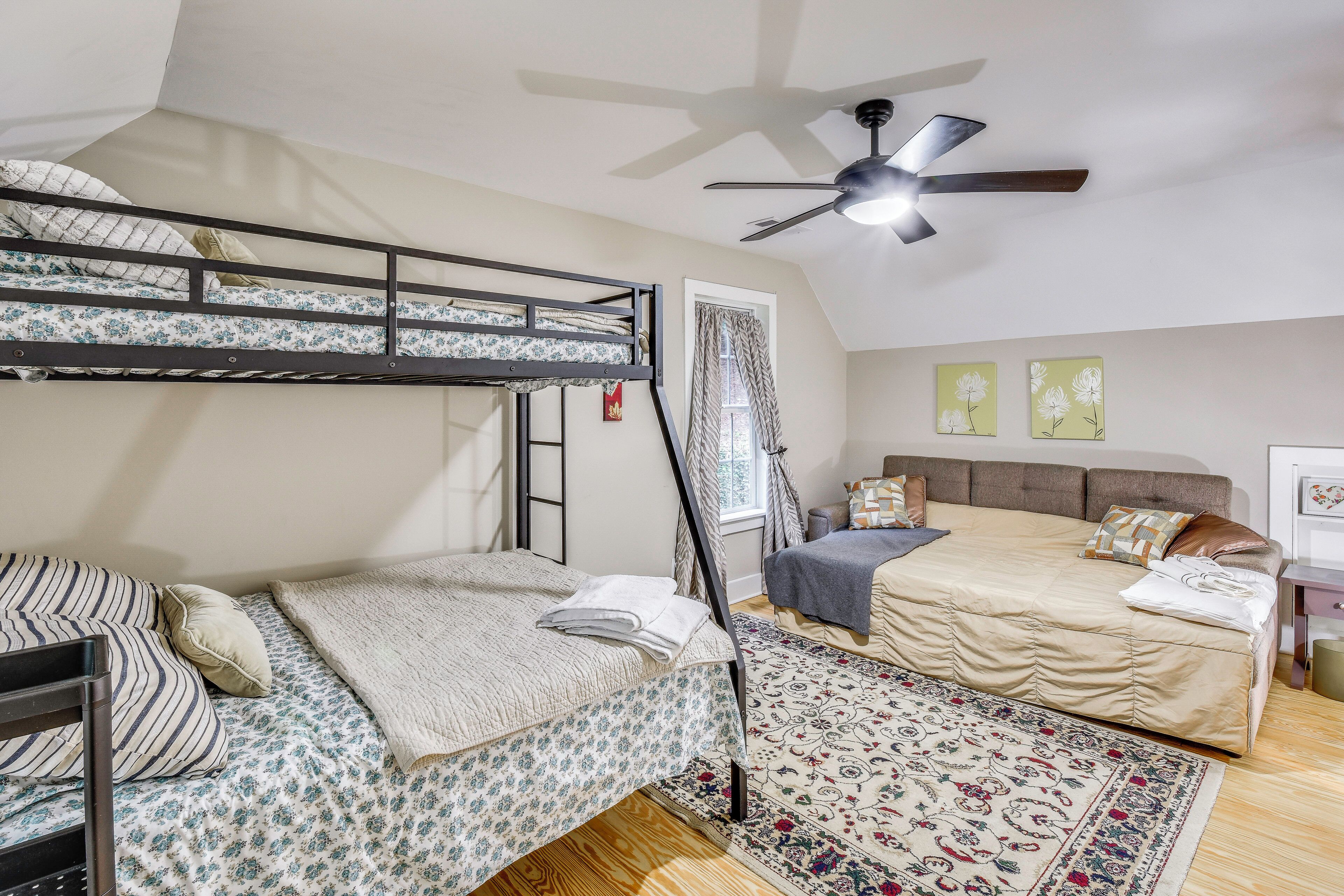 A dorm-style room with bunk beds, a ceiling fan, a window with curtains, and a bed with a patterned rug.