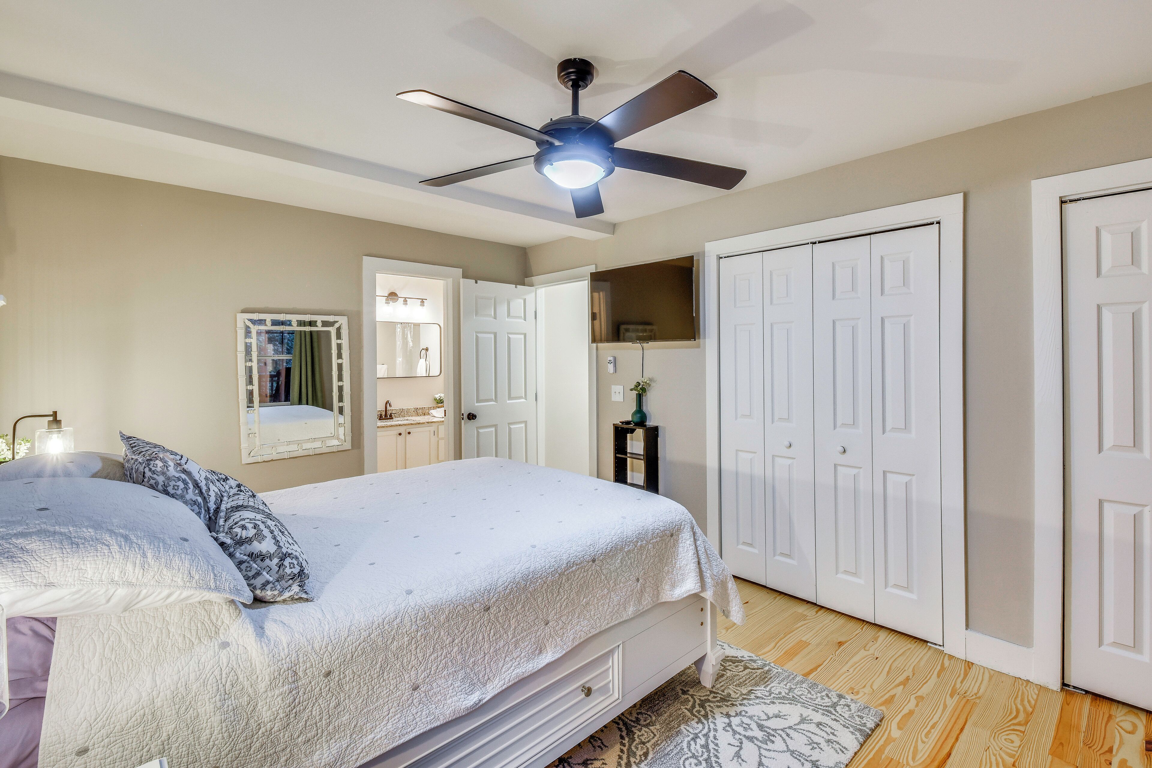 A bedroom with a bed, a ceiling fan, a mirror, and white doors.