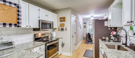 A modern kitchen with white cabinets, a microwave, a stove, and a sink.