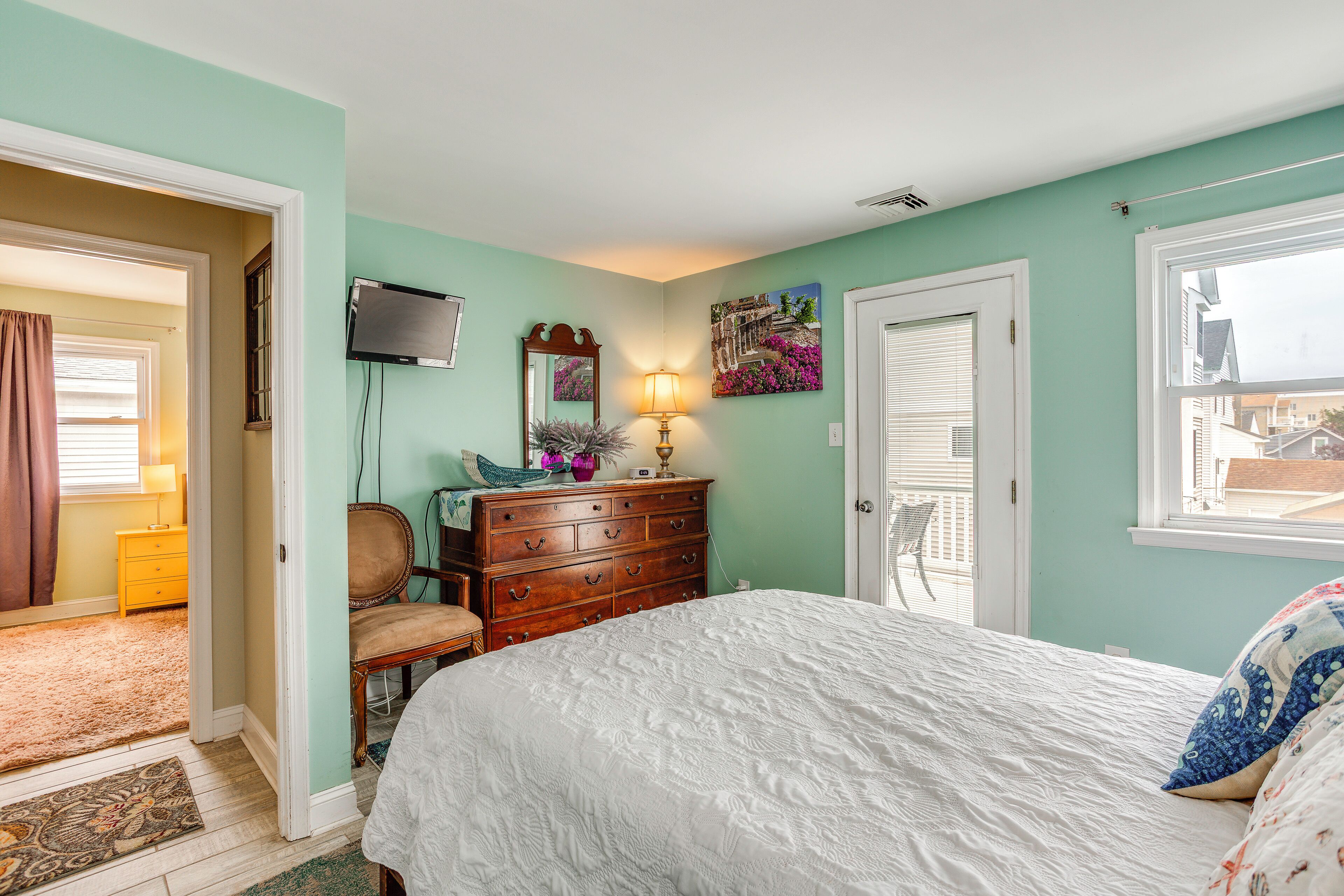 A bedroom with a bed, dresser, chair, and artwork on the wall.
