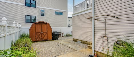 A residential backyard with a gravel path, a wooden shed, and a white fence.