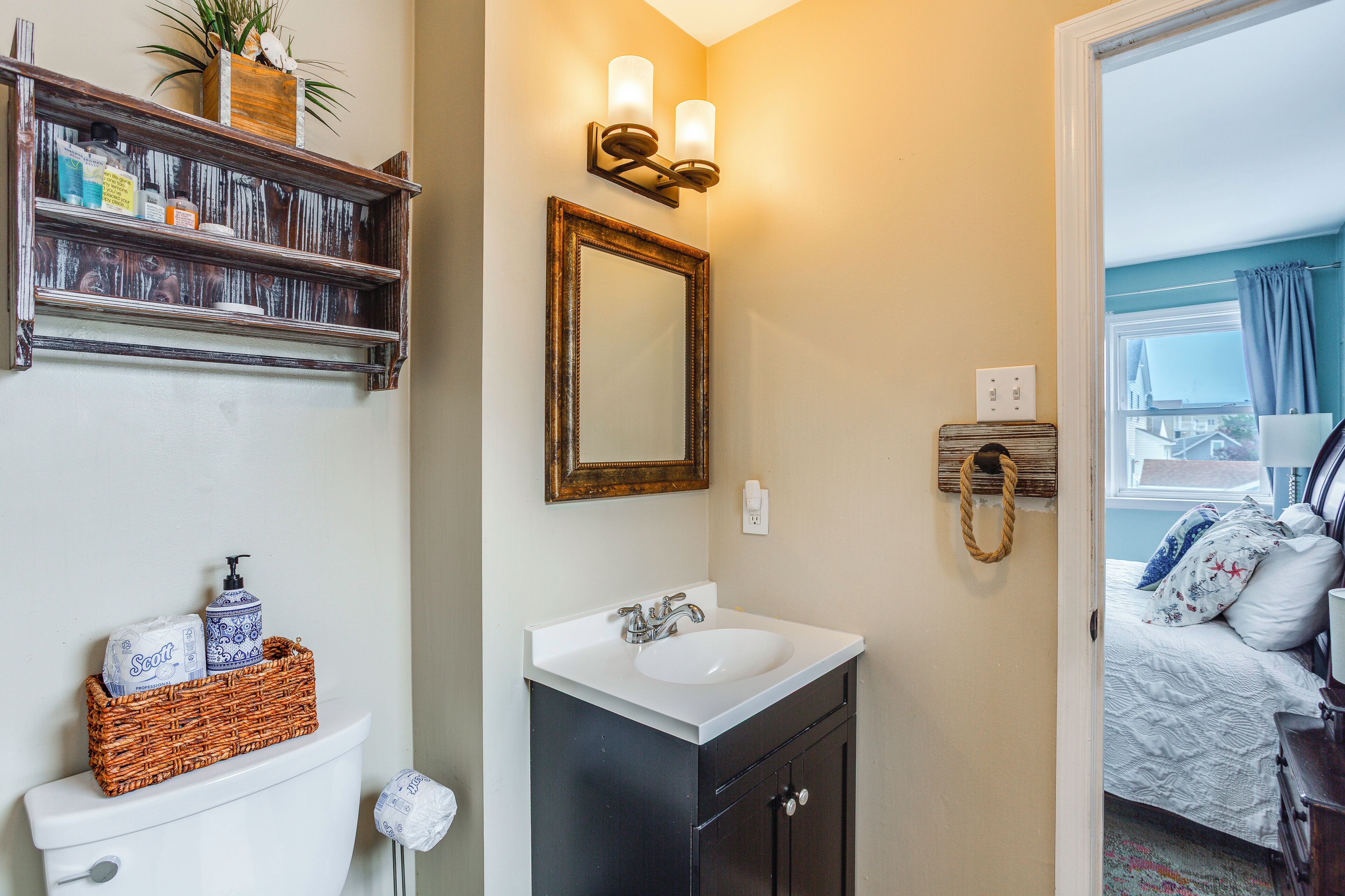 A bathroom with a white sink, dark cabinets, a mirror, and a shelf with toiletries.