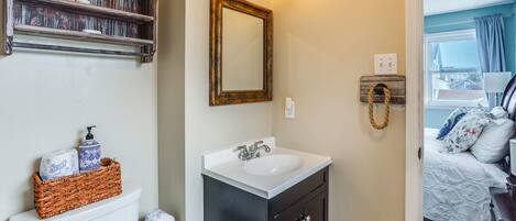 A bathroom with a white sink, dark cabinets, a mirror, and a shelf with toiletries.