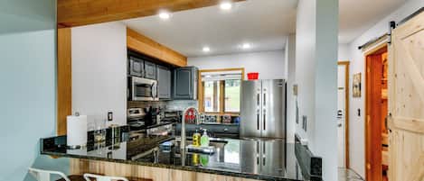 A kitchen with a central island, bar stools, stainless steel appliances, and a wooden ceiling.