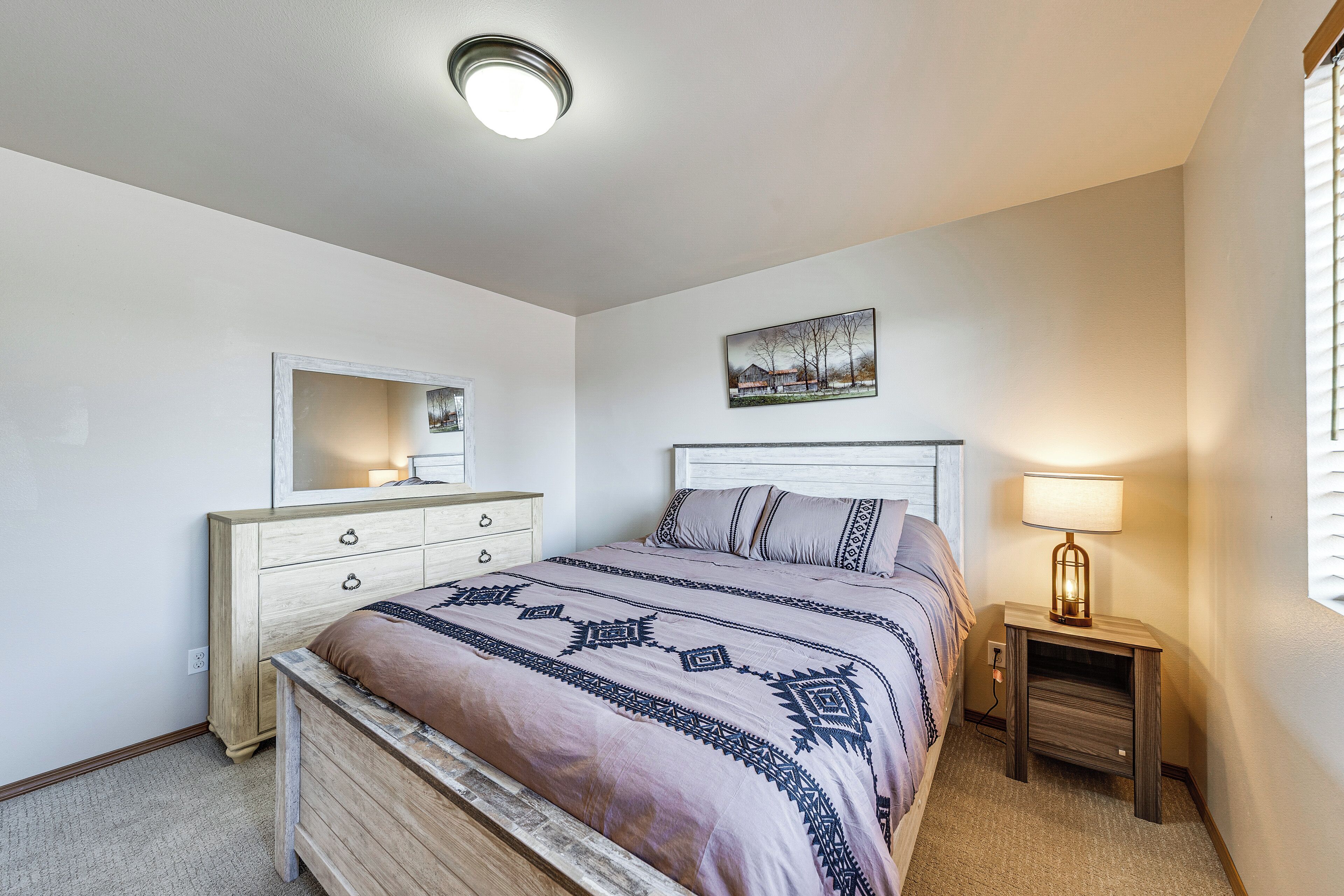Une chambre à coucher comprenant un lit, une commode, une table de chevet, une lampe et un tableau accroché au mur.