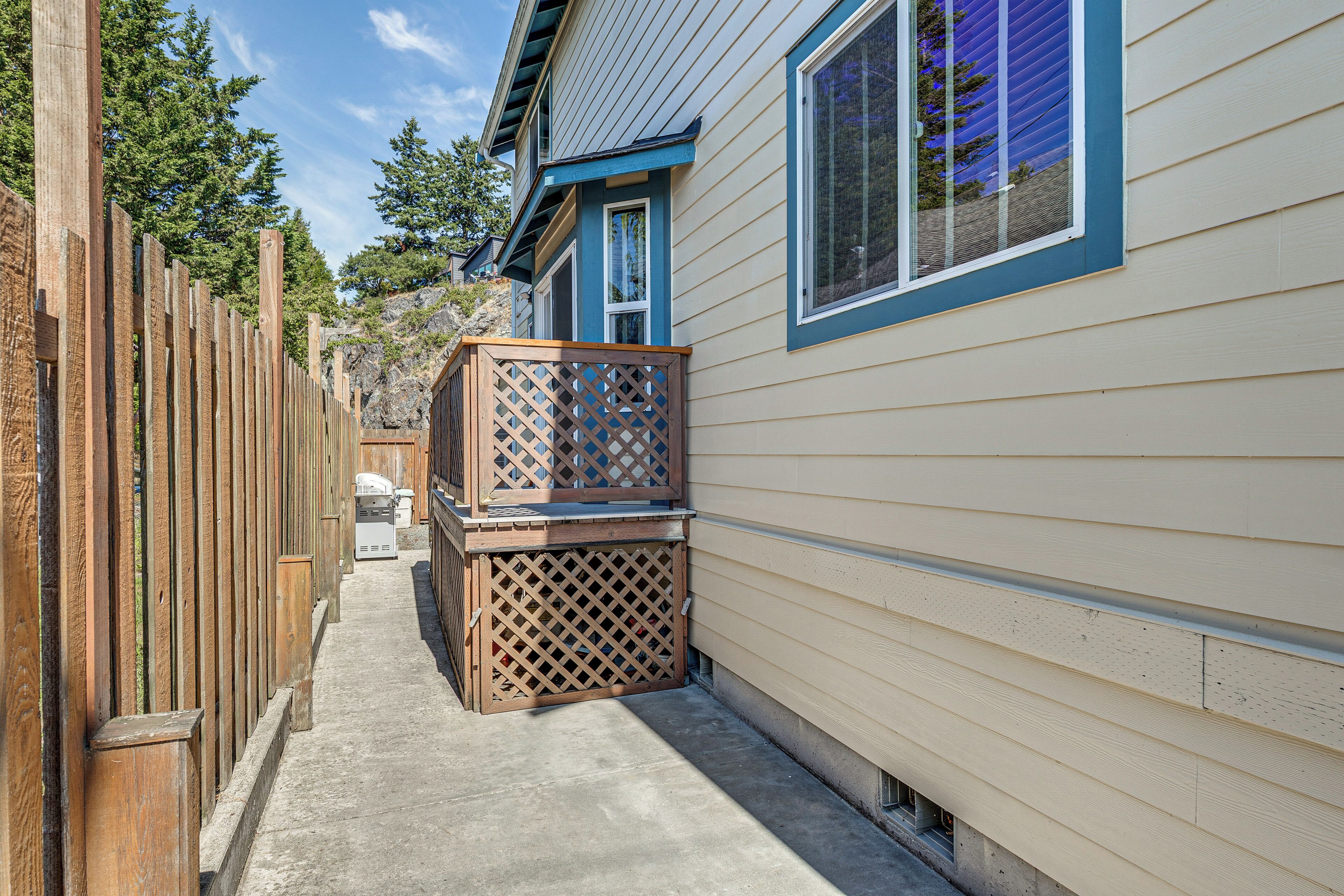 A narrow outdoor pathway leading to a house with a wooden fence on one side and a deck with a lattice screen on the other.