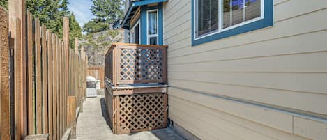 A narrow outdoor pathway leading to a house with a wooden fence on one side and a deck with a lattice screen on the other.