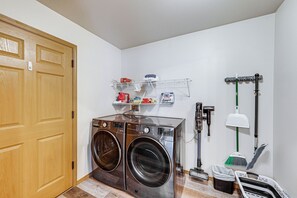 Ein Waschraum mit zwei Waschmaschinen, einem Wäscheständer, einem Besen, einem Mop und einem Mülleimer.