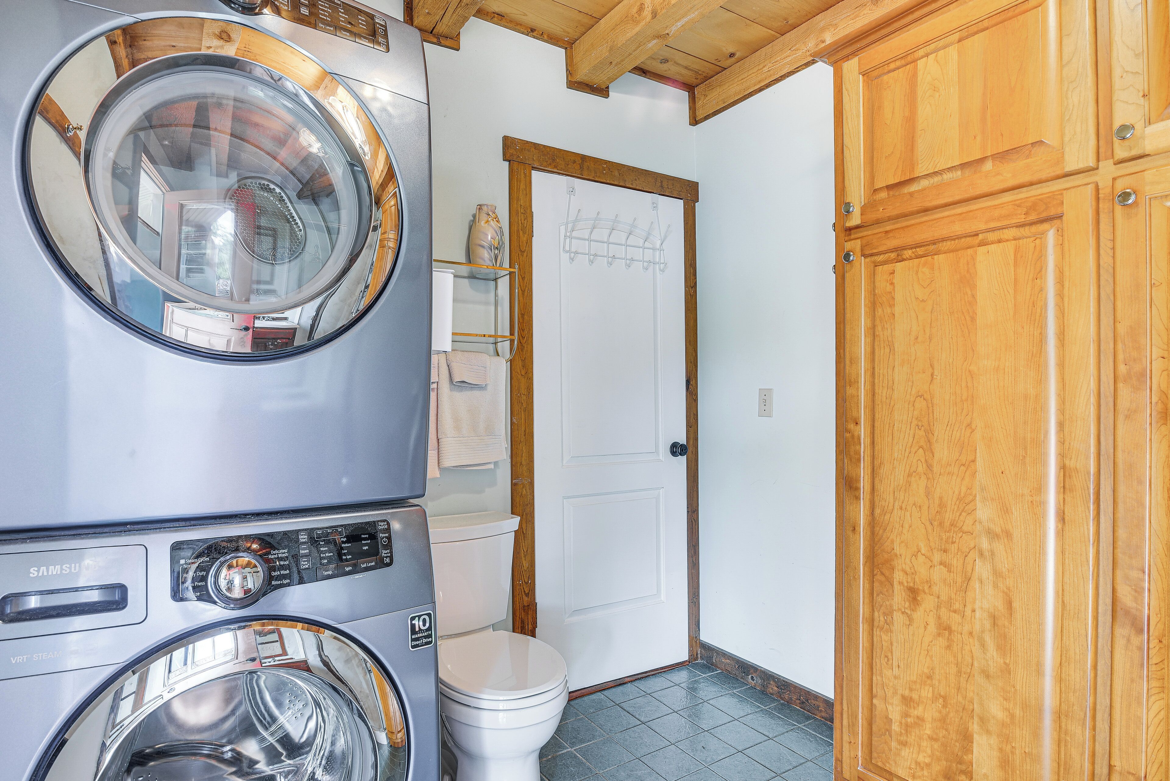 A laundry room with stacked washers and dryers, a white toilet, and wooden cabinets.
