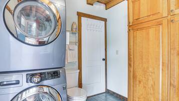 A laundry room with stacked washers and dryers, a white toilet, and wooden cabinets.
