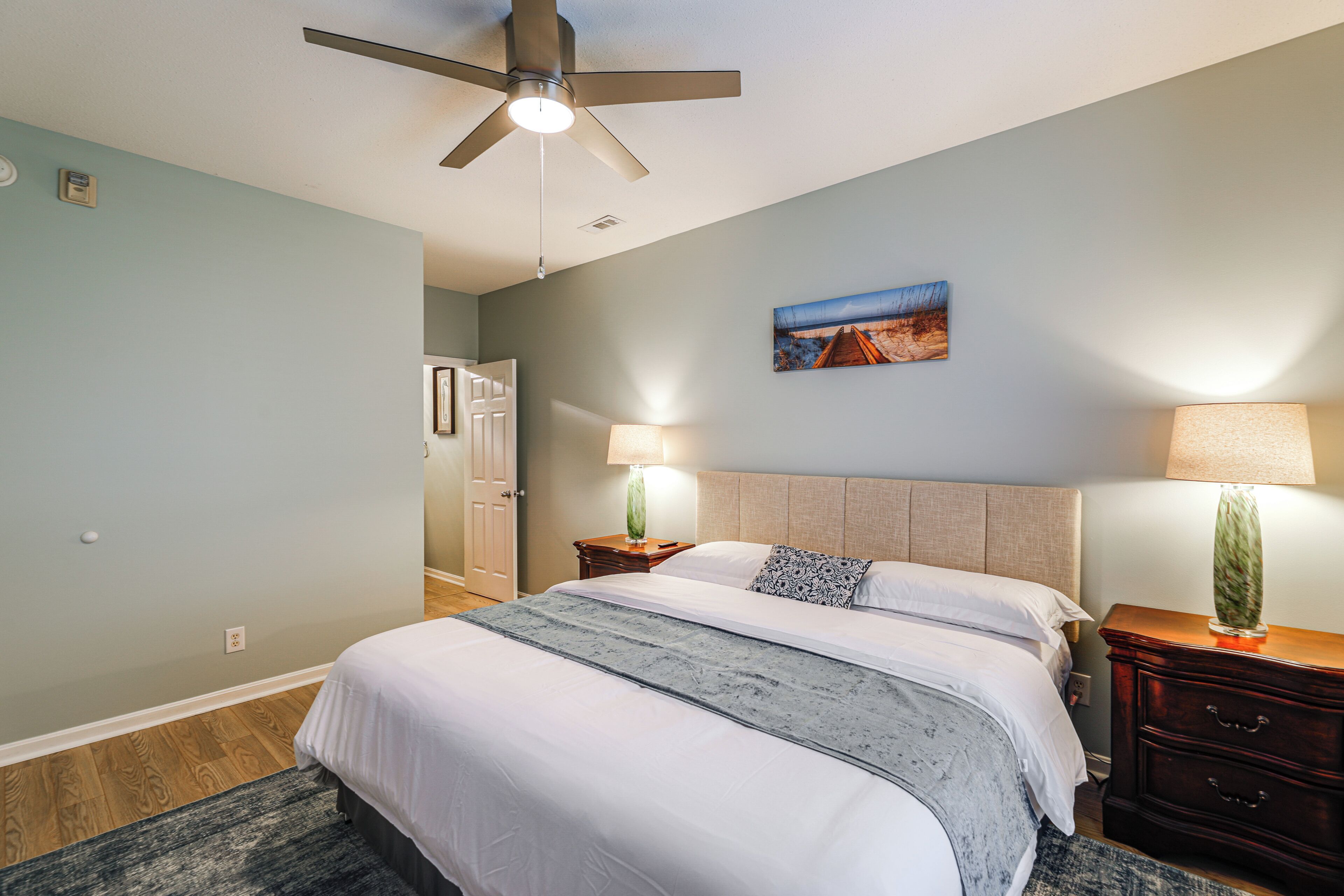 A hotel room with a bed, bedside lamps, a painting, and a ceiling fan.