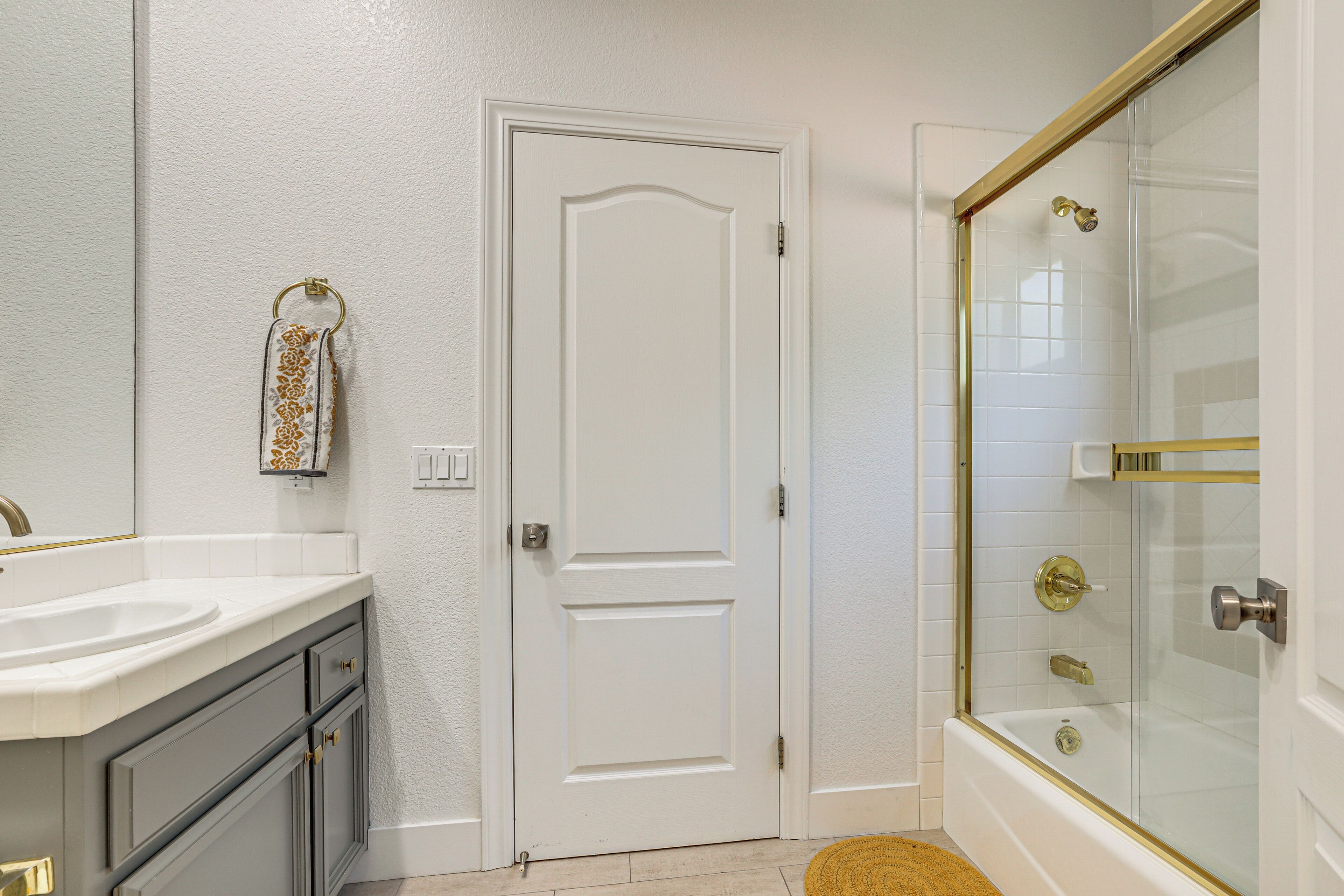 A bathroom with a white door, a glass shower enclosure, and a sink with a gold faucet.