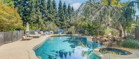 Una piscina con deck de piedra, sillas de descanso y una cascada pequeña.
