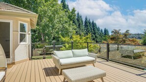 A deck with a wicker sofa and ottoman, a glass door, and a view of trees and hills.