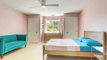 Um quarto com cama, janela, ventilador de teto e um sofá azul-esverdeado.