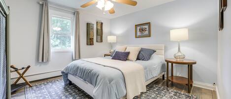A bedroom with a bed, a ceiling fan, a window with curtains, a nightstand, and a lamp.