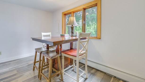 A dining area with a wooden table, two chairs, a lamp, and a window with a view of trees. - Creekside Retreat in Speedsville w/ Deck & Yard (Berkshire)