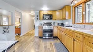 A kitchen with wooden cabinets, a stove, a microwave, and a large window. - Creekside Retreat in Speedsville w/ Deck & Yard (Berkshire)
