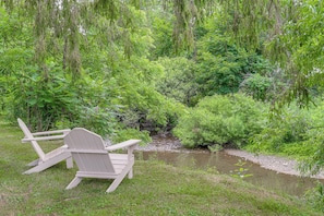 A wooden chair and table set up by a stream in a lush green area. - Creekside Retreat in Speedsville w/ Deck & Yard (Berkshire)