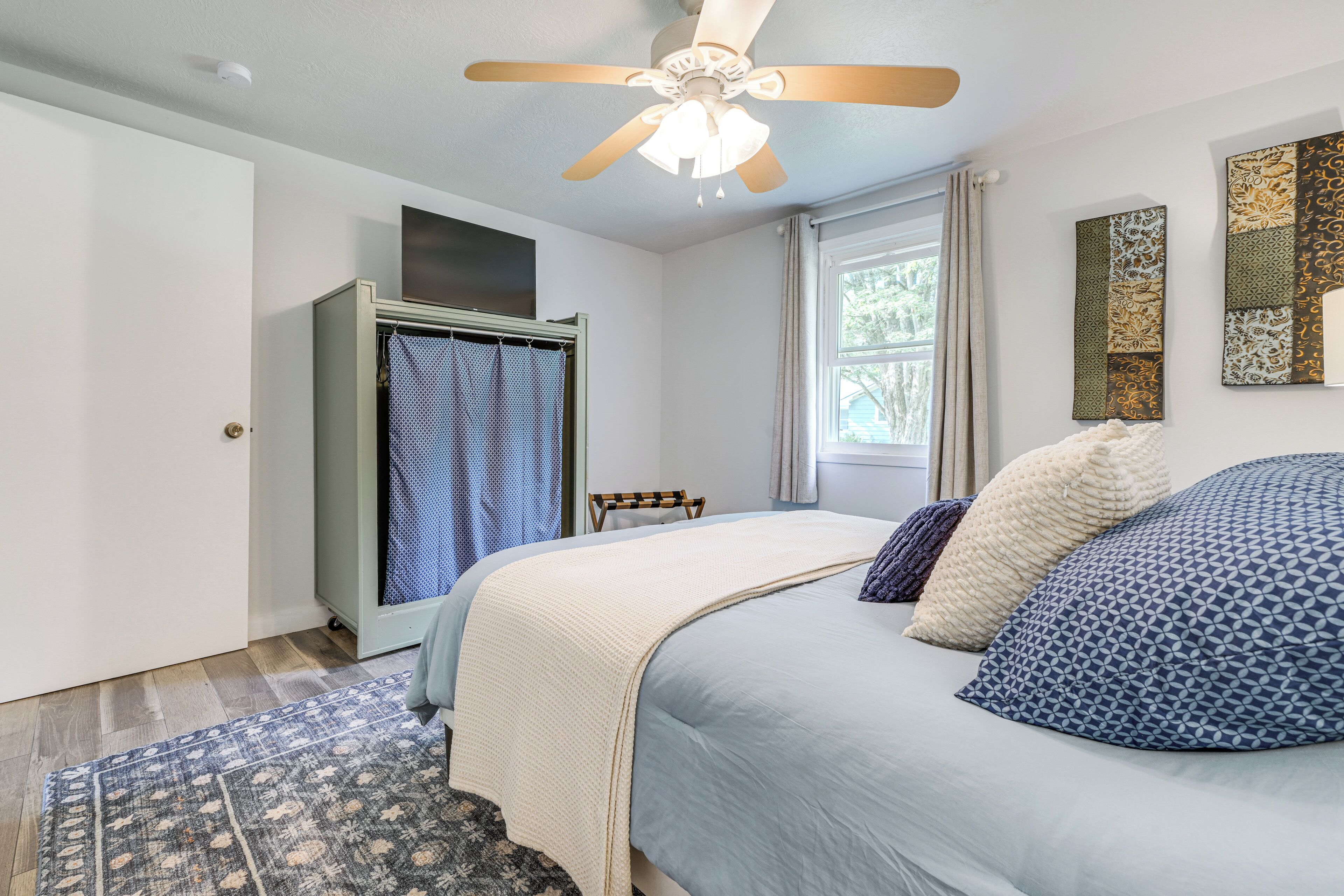 A bedroom with a bed, a ceiling fan, a wardrobe, a window with curtains, and a rug.