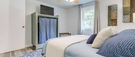 A bedroom with a bed, a ceiling fan, a wardrobe, a window with curtains, and a rug.