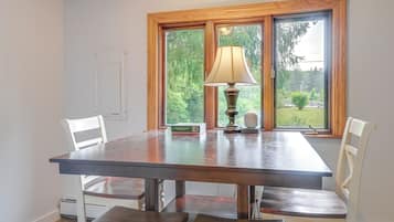 A dining table with chairs, a lamp, and a window with a view of greenery.