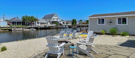 A waterfront patio with Adirondack chairs, a small table, and a stone deck.