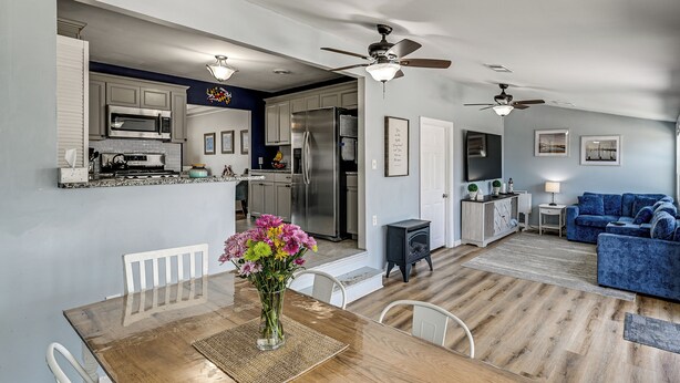 A modern kitchen with stainless steel appliances, a dining area with a wooden table and white chairs, and a living room with a blue sofa.
