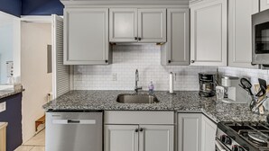 A kitchen with white cabinets, a granite countertop, a stainless steel sink, a coffee maker, and a stove.
