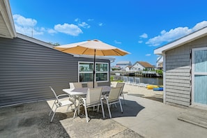 Eine Terrasse mit Tisch und Stühlen, einem großen Sonnenschirm und Blick auf ein Gewässer mit Booten.