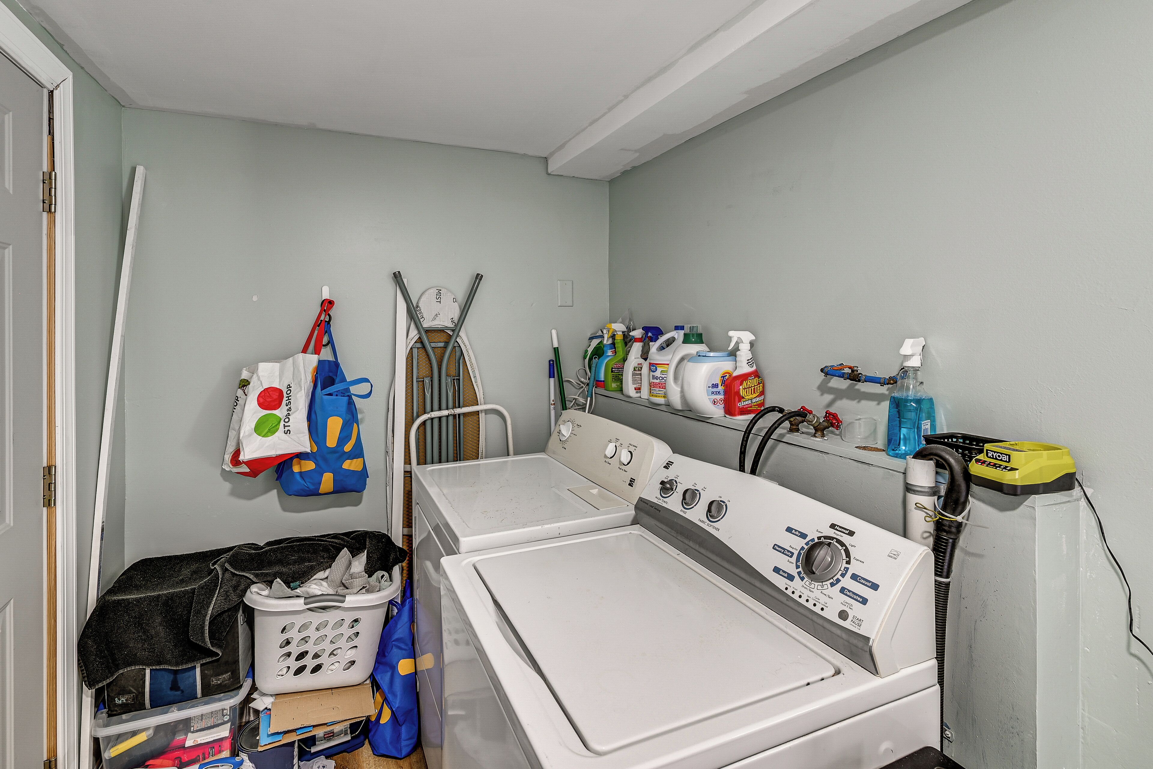 A laundry area with a washing machine, dryer, and a hose. There are cleaning supplies on a shelf.