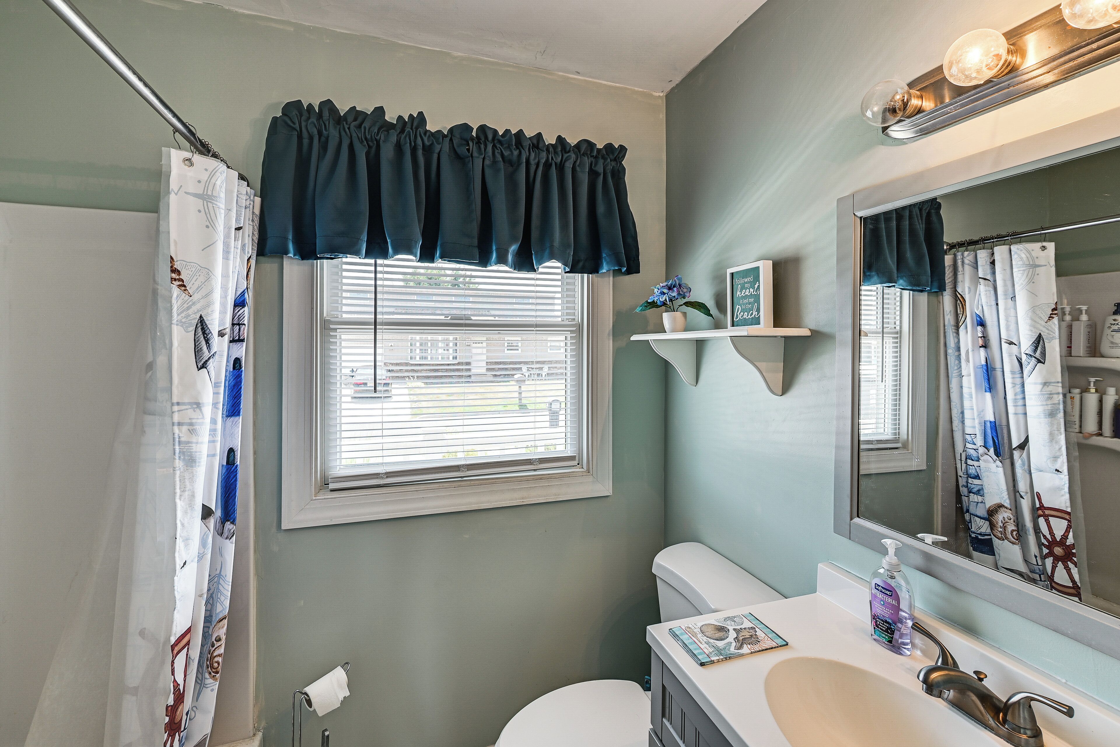 A bathroom with a toilet, sink, mirror, and window with blinds.
