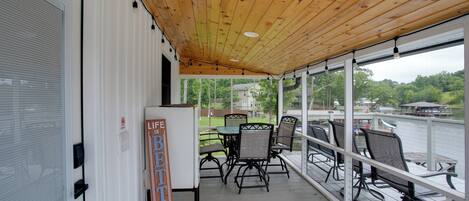 A covered outdoor seating area with a wooden ceiling, a refrigerator, and a sign that reads 'Life Better at the Lake.'