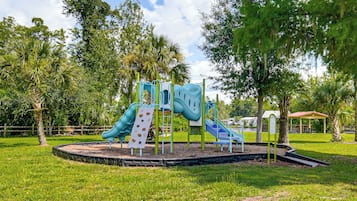A playground with slides and climbing structures surrounded by grass and trees.