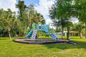 A playground with slides and climbing structures surrounded by grass and trees.