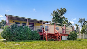 A two-story house with a red staircase leading to a porch, surrounded by a grassy yard and trees.