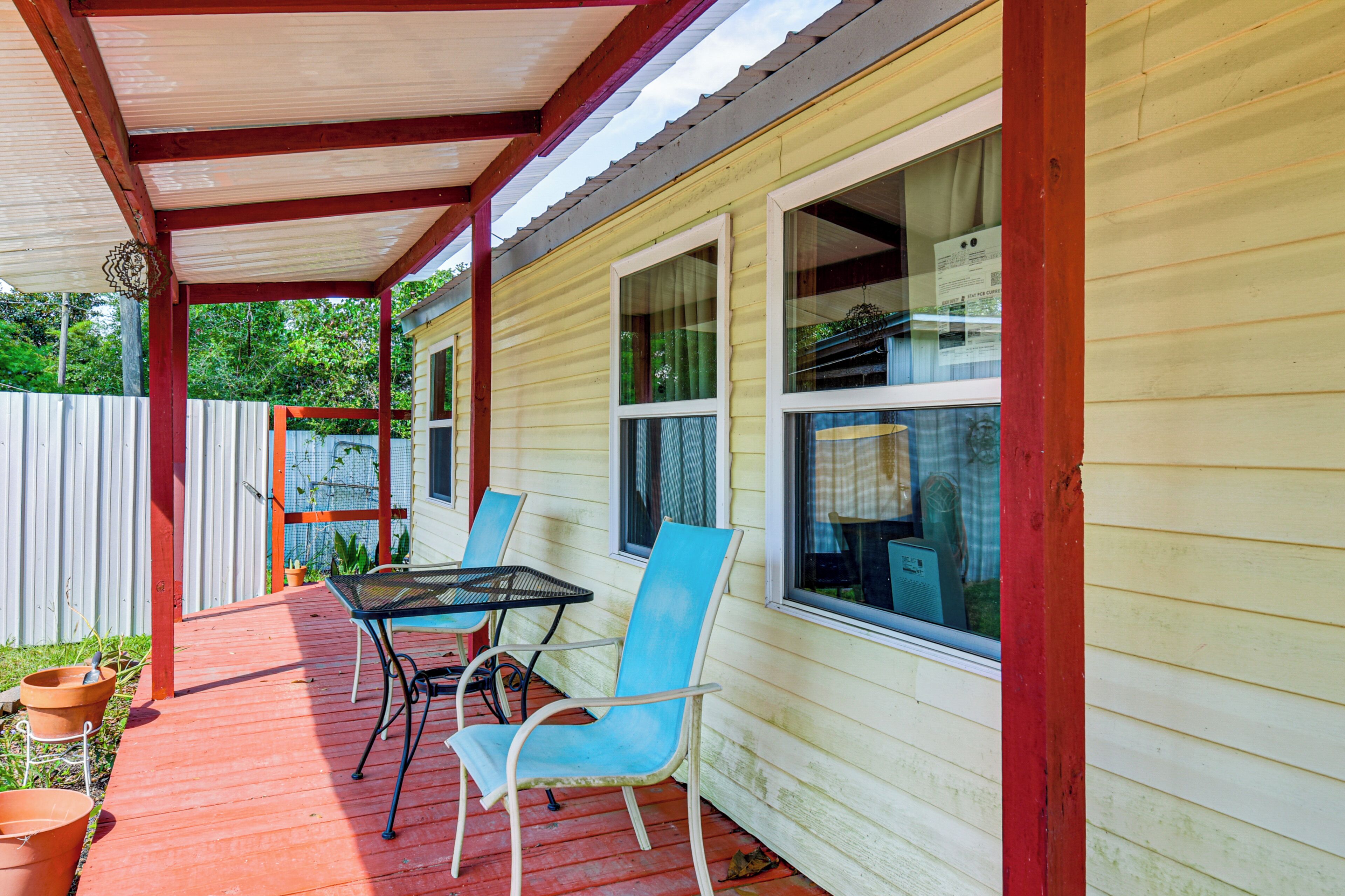 A covered patio with a table and chairs, a wooden deck, and a white fence.