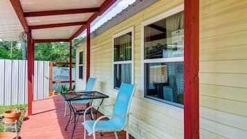 A covered patio with a table and chairs, a wooden deck, and a white fence.