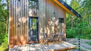 A wooden cabin with a deck, a door, and two windows. - Modern PNW Cabin on 10 Wooded Acres (Warren)